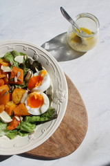 Roasted veggie salad. Oven baked butternut squash, lettuce, boiled egg and mixed seeds salad on a vintage white plate served on top of a wooden table. Healthy and colourful salad. Top view. 