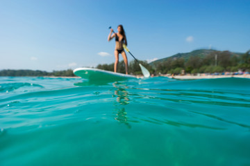 Stand up paddle board woman paddleboarding .Selective focus on water. Woman and beach blured.