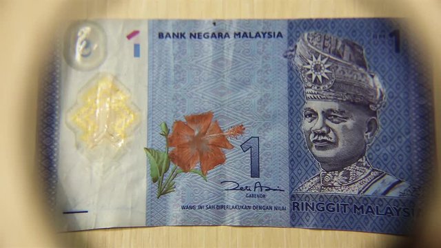 View a One Malaysian ringgit bill lying on a table with a magnifying glass. concept of business and finance.
