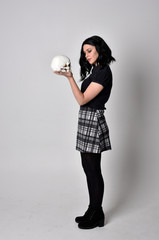  Portrait of a goth girl with dark hair wearing blue and plaid skirt with boots. Full length...