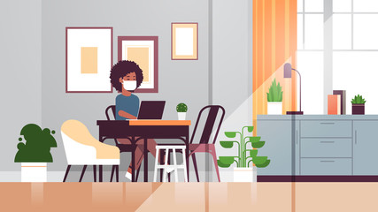 african american woman in protective mask using laptop coronavirus pandemic quarantine concept work from home online education freelance modern living room interior full length horizontal vector