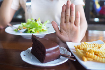 The hands of women care for health and diet, pushed from the chocolate cake and french fries plate. And choose eat vegetable or salad that contains vitamins and helps control weight for a slim stock.