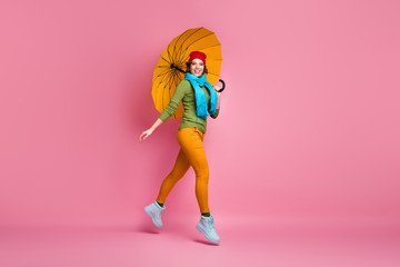 Full size photo of cheerful sweet cute girl jump enjoy go walk hold bright parasol wear blue red headwear sweater trousers footwear isolated over pink color background