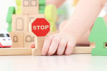 caucasian boy sets a stop road sign on the background of the children's kit of a wooden toy city....
