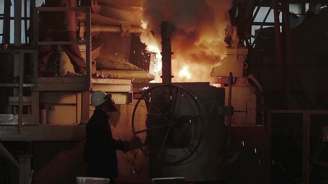 Room for the manufacture of metal products by casting. Casting shop for gassified models. The molten metal is poured from the induction furnace into the ladle. Sparks of hot metal fly apart.