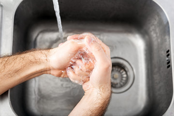 Fototapeta premium Man washing hands with antibacterial soap and water in metal sink for corona virus prevention. Hand hygiene, health care, medical concept. Hand skin disinfection protect from Coronavirus covid 19
