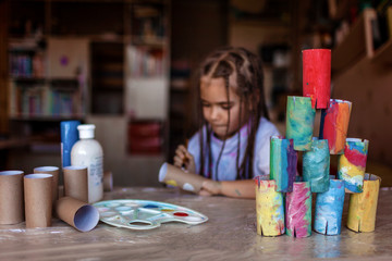 Cute girl coloring toilet paper rolls to use them like paper blocks to build a tower