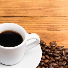 Freshly made coffee in a white cup surrounded by coffee beans on a wooden table. Fresh roasted coffee.