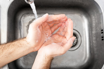 Fototapeta premium Man washing hands with antibacterial soap and water in metal sink for corona virus prevention. Hand hygiene, health care, medical concept. Hand skin disinfection protect from Coronavirus covid 19