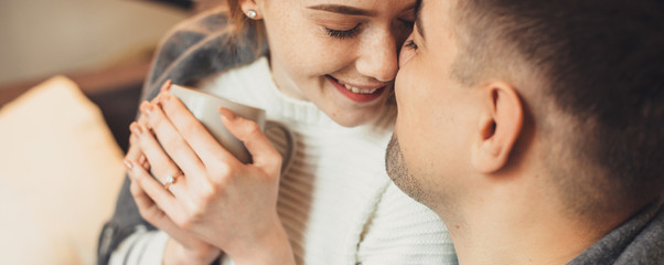 Fototapeta premium Lovely caucasian girl with freckles and red hair is drinking a tea while cheering on a sofa with her lover
