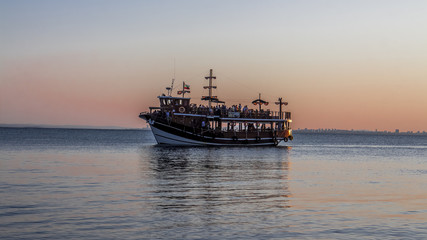 A group of people sail on a small ship. They will never forget the enjoyment of the beautiful view of the sunset in the sea. Golden hour of happiness in Pomorie, Black Sea / Bulgaria. Summer season.