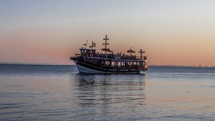 Fototapeta premium A group of people sail on a small ship. They will never forget the enjoyment of the beautiful view of the sunset in the sea. Golden hour of happiness in Pomorie, Black Sea / Bulgaria. Summer season.