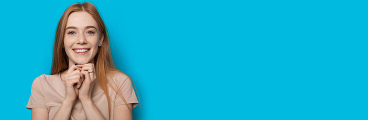 Sweet caucasian woman with red hair and freckles smiling at camera on a blue wall with freespace