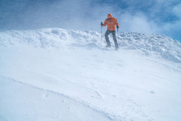  High mountaineer dressed bright orange softshell jacket using a trekking poles descending the...
