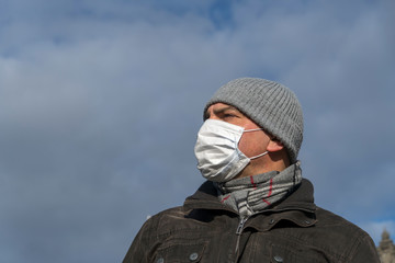 Disease outbreak, coronavirus covid-19 pandemic. Close up portrait from below of a man posing outdoors protecting his face with a mask