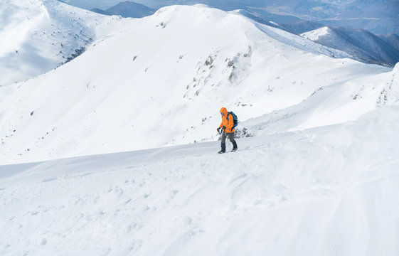  High mountaineer dressed bright orange softshell jacket using a trekking poles ascending the snowy mountain summit. Active people concept image on Velky Krivan, SLovakian Tatry.