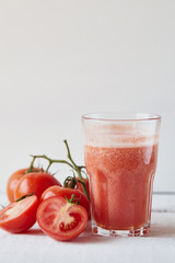 Tomatoes fresh juice in the glass with ingredients on the light background