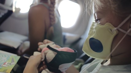 Little girl caucasian at plane with wearing protective medical mask. Child baby tourist at aircraft...