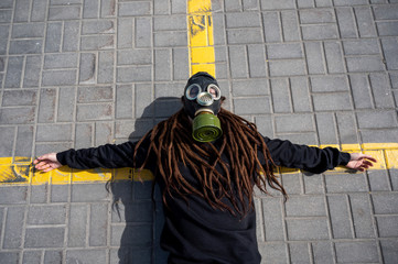girl with dreadlocks in a gas mask lies arms outstretched in the parking lot