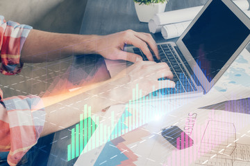 Double exposure of stock graph with businessman typing on computer in office on background. Concept of hard work.