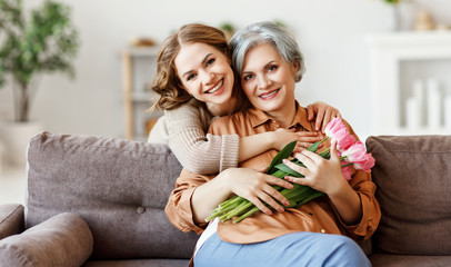 Happy woman hugging aged mother with flowers.