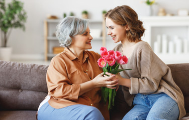 Young woman giving flowers to senior mother.