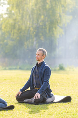 Naklejka na ściany i meble A young man meditates outdoors in a park. 