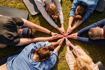 Close up of hands of people sitting outdoors on green grass after doing yoga