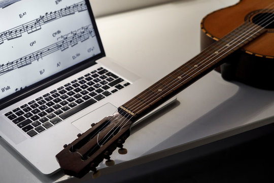 Chitarra poggiata sopra un compuetr portatile e sullo schermo spartiti di musica 