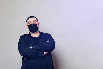 man in black shirt and black hospital mask on gray wall background
