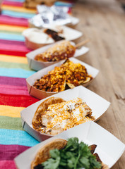 Street food festival. Mexican food takeaway.  Many tacos in carton boxes on wooden table. Outdoor lunch. Vegan and healthy.