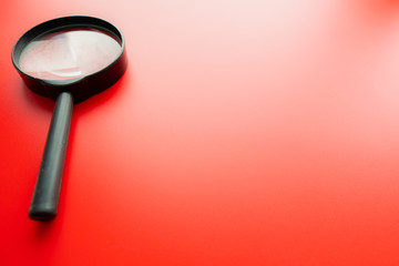 Close up Single Magnifying Glass with Black Handle, Leaning on the red Table at the Office.