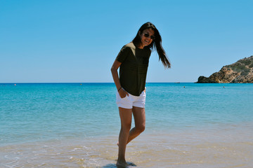 Caucasian woman in white shorts and dark t-shirt standing on a beach in a summer