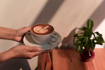 Hand holding latte or Cappuccino with frothy foam, coffee cup in cafe.