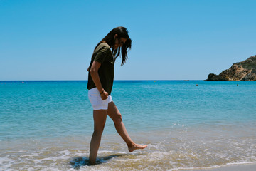 Caucasian woman in white shorts and dark t-shirt standing on a beach in a summer
