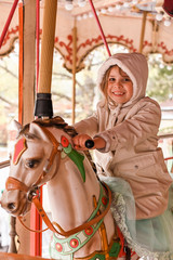 Fototapeta na wymiar Little girl rides a carousel in an amusement park. Happy child.