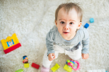 Portrait of one year old baby girl indoors in bright room siting on a carpet.