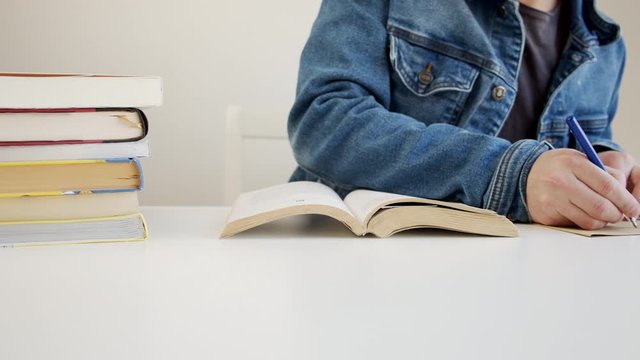 Male studying at home during the quarantine writes a quote from a book on a paper