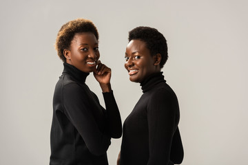 smiling african american girls in black turtlenecks isolated on grey