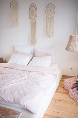 Bed with pink and white cotton sheets in a room decorated with dream catchers