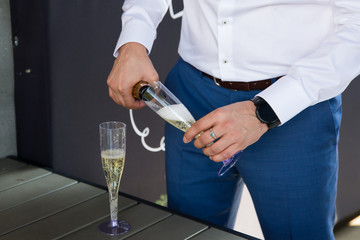  Groom pours champagne into a glass. 2 glasses with champagne. Wedding