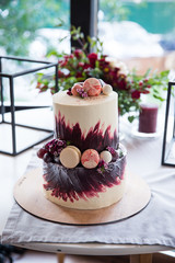 Two tiered white-burgundy wedding cake decorated with macaroons, grapes and flowers