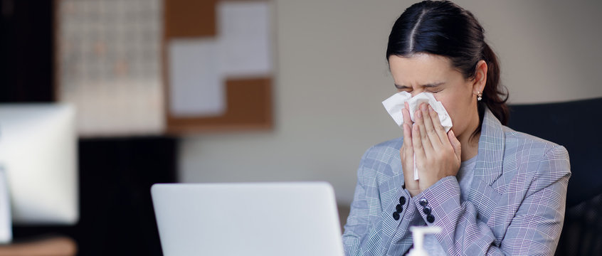 Sick, ill unhealthy female employee coughing or sneezing while working in workplace in office. Spreading and risk of corona virus covid-19 in workplace.