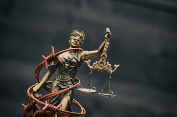 Scales of Justice, Justitia, Lady Justice and barbed wire on a black wooden background.