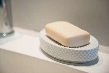 Yellow hand soap in a white ceramic soap dish sitting on a modern white sink selective focus.
