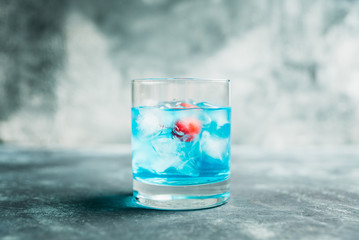 Blue old fashioned cocktail with cherry on the rustic background. Selective focus. Shallow depth of field.