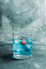Blue old fashioned cocktail with cherry on the rustic background. Selective focus. Shallow depth of field.