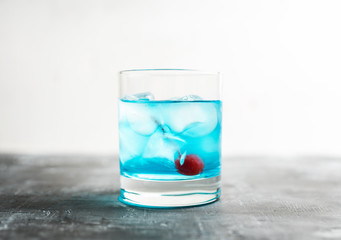 Blue old fashioned cocktail with cherry on the rustic background. Selective focus. Shallow depth of field.