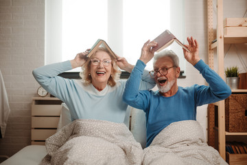 Good looking elderly couple wearing pajamas enjoying their time together lying in bed. They are...