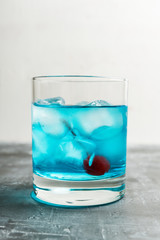 Blue old fashioned cocktail with cherry on the rustic background. Selective focus. Shallow depth of field.